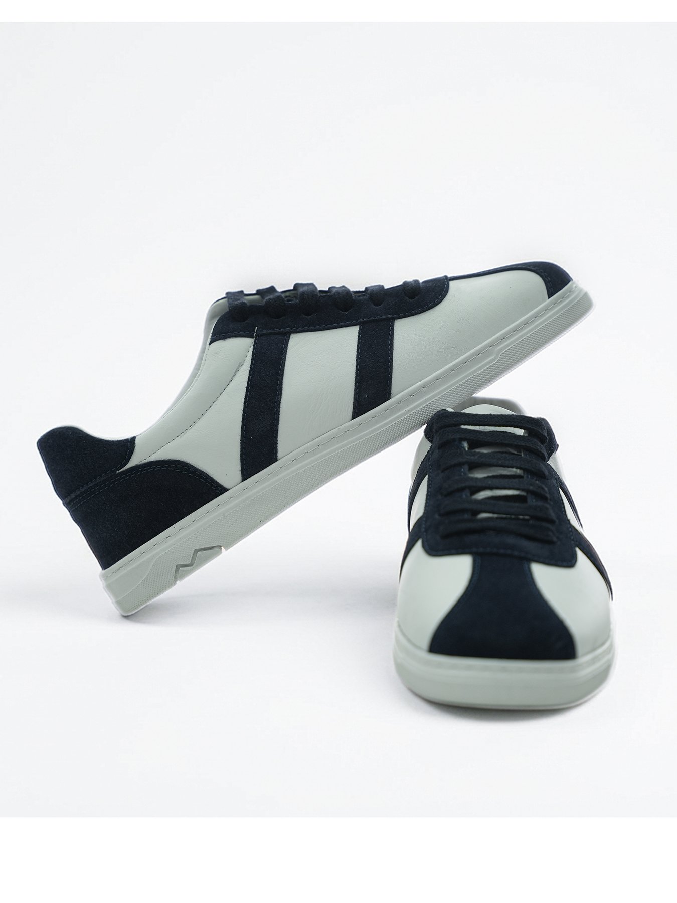 Beyaz deri ve lacivert süet detaylara sahip low-top erkek günlük sneaker çiftinin önden ve yandan sergilendiği dinamik ürün çekimi